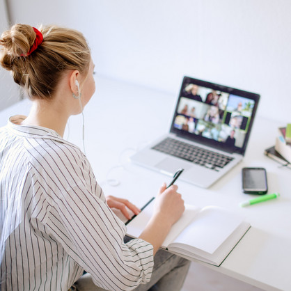Digitales Lernen Am Schreibtisch sitzende Studentin schaut Lernvideos, daneben liegen Bücher und Stifte.